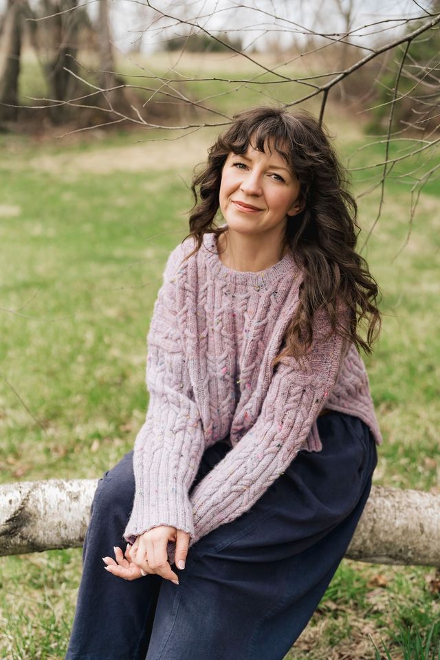 Woman sitting on a log in a natural setting wearing a pink sweater.