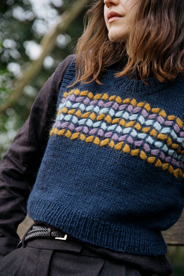 Person wearing a blue knitted sweater with colorful pattern, outdoors.