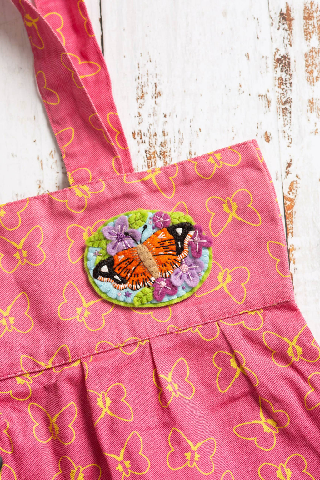 Pink apron with butterfly pattern and embroidered patch on a wooden surface