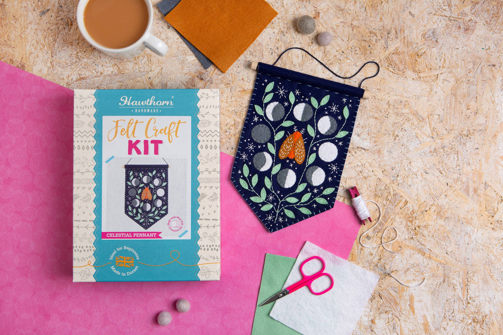 Felt craft kit with a completed project, cup of coffee, and sewing tools on a textured surface.