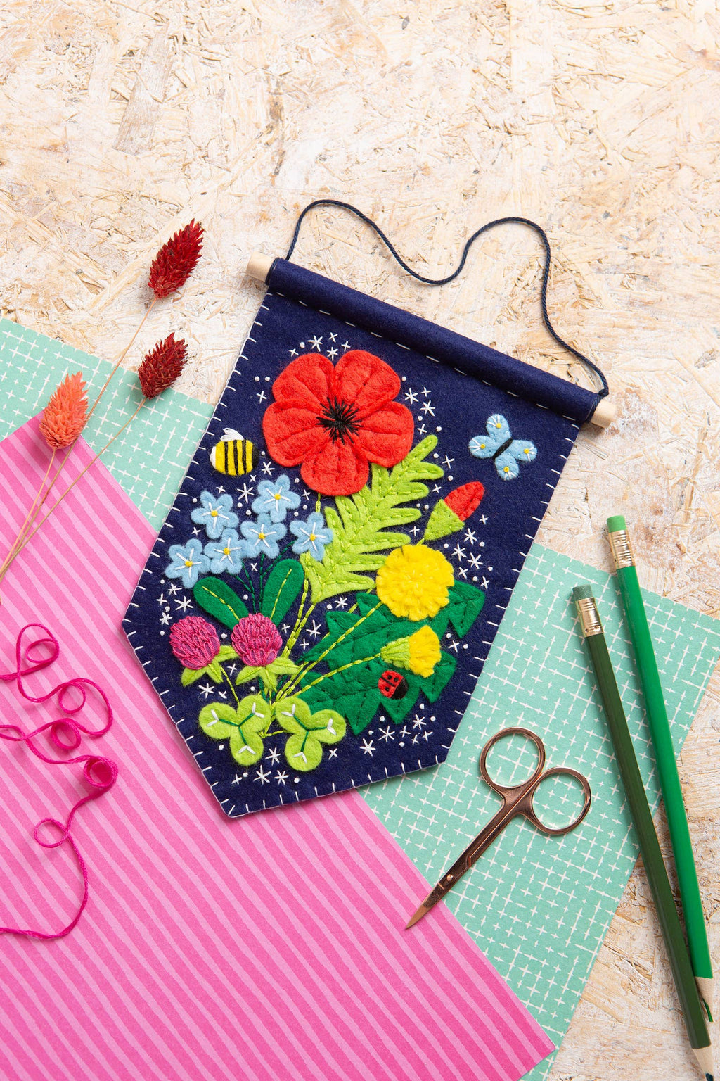 Embroidered wall hanging with colorful flowers on a textured surface with crafting tools.