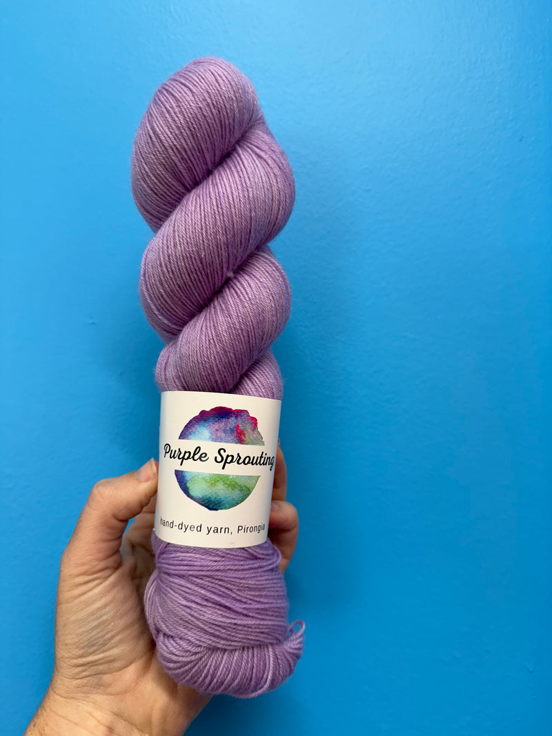Purple skein of yarn held against a blue background with a visible label.